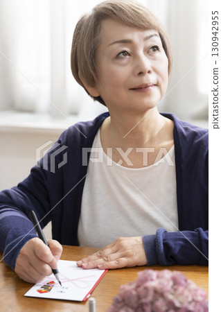 A senior woman writing the address on a gift envelope with a brush pen 130942955