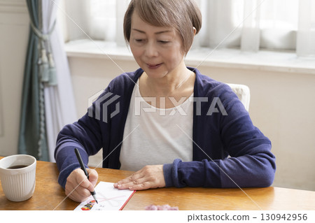 A senior woman writing the address on a gift envelope with a brush pen 130942956