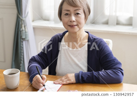 一位老年婦女用毛筆在禮物信封上寫地址 一位老年婦女用毛筆在禮物信封上寫地址 130942957