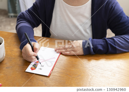 A senior woman writing the address on a gift envelope with a brush pen A senior woman writing the address on a gift envelope with a brush pen 130942960
