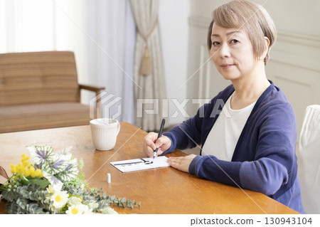 A senior woman writing the address on a condolence envelope with a brush pen 130943104
