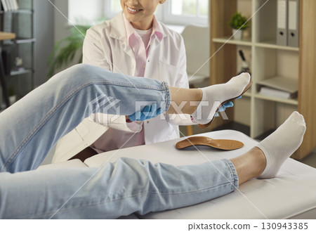 Cheerful female orthopedist fitting insole on patient's foot lying on couch in medical clinic. 130943385