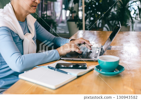 Confident senior woman smiling during phone call at cozy workspace with coffee 130943582