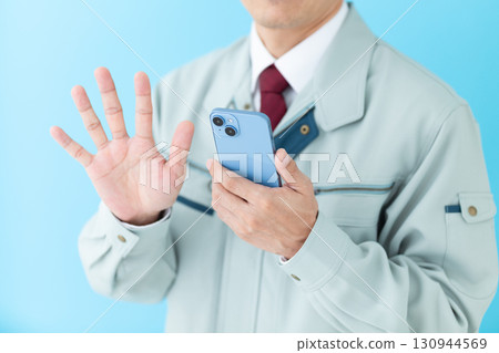 一位身穿工作服的中年男性商人拿著智慧型手機，用五根手指指著 130944569