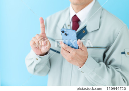 A middle-aged male businessman in work clothes holding a smartphone and pointing his index finger 130944720