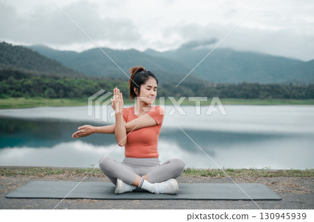 Woman in yoga pose by a tranquil lake with mountains, showcasing outdoor fitness and mindfulness. Woman in yoga pose by a tranquil lake with mountains, showcasing outdoor fitness and mindfulness. 130945939