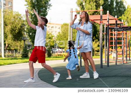 Family Chases Bubbles as Mom Blows Them at Playground 130946109