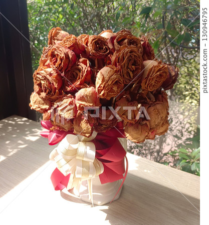 A bouquet of dried roses, brown and red, in a vase, tied with red and white ribbons, on table, nature background, love, valentine, decor, fashion, copy space 130946795