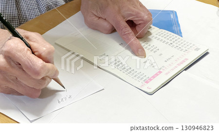 The hand of an elderly woman opening her bankbook, pointing and writing notes The hand of an elderly woman opening her bankbook, pointing and writing notes 130946823