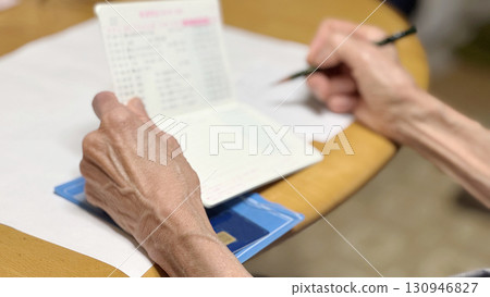Hands of an elderly woman opening her bankbook and writing notes 130946827