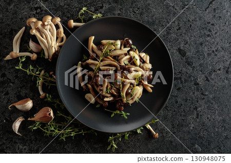 Fried shimeji mushrooms with thyme and garlic on a black plate. Fried shimeji mushrooms with thyme and garlic on a black plate. 130948075