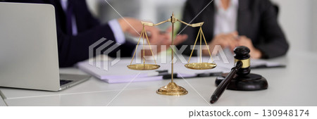 Legal professionals discussing justice system ethics and law in office setting with scales gavel laptop paperwork during important consultation 130948174