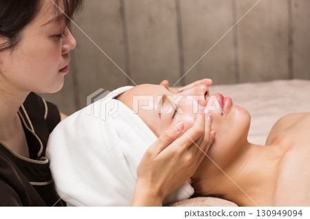 Young asian beautician doing facial massage. 130949094
