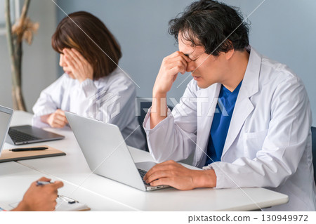 Overwork, fatigued male doctor holding his head, doctor (poor health, lack of sleep, doctor shortage, stress) Overwork, fatigued male doctor holding his head, doctor (poor health, lack of sleep, doctor shortage, stress) 130949972