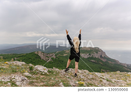 A woman is standing on a mountain top, looking out over the ocean A woman is standing on a mountain top, looking out over the ocean 130950008