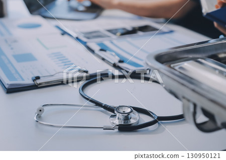 Two doctors and a female nurse meet at a table in the hospital, collaborating on medical tasks using laptops and computers Two doctors and a female nurse meet at a table in the hospital, collaborating on medical tasks using laptops and computers 130950121