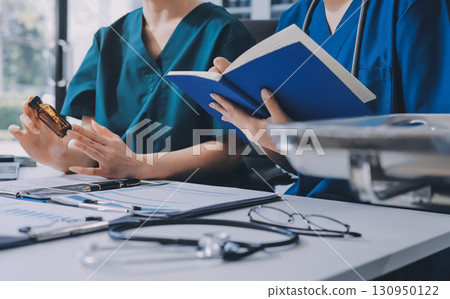 Two doctors and a female nurse meet at a table in the hospital, collaborating on medical tasks using laptops and computers 130950122