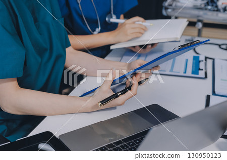 Two doctors and a female nurse meet at a table in the hospital, collaborating on medical tasks using laptops and computers 130950123