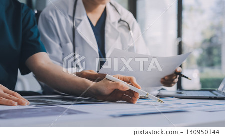 Medical team meeting analyzing blood test results in hospital laboratory. Doctors and scientists in lab coats are having a discussion about blood test result, holding test tubes and taking notes. 130950144