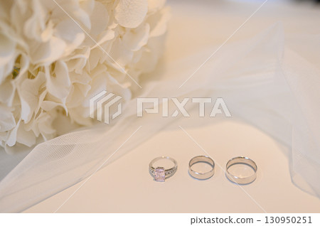 Wedding rings and engagement ring displayed with white hydrangeas and veil, symbolizing love, commitment, celebration of marriage 130950251