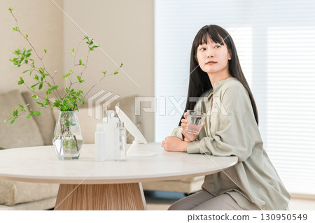 A young Asian, Japanese woman drinking mineral water, water, hot water in a glass in the living room in the morning (detox) 130950549