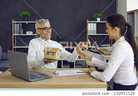 Male real estate agent in office meeting hands over keys to his new home to happy young woman. 130951526