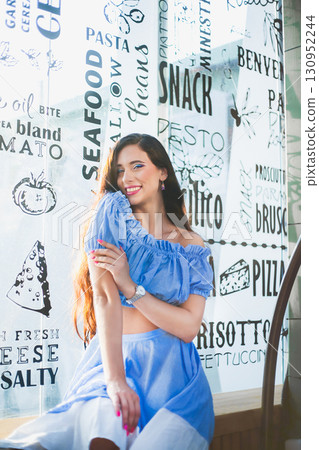 Woman in blue outfit posing happily by restaurant menu window in bright daylight Woman in blue outfit posing happily by restaurant menu window in bright daylight 130952244