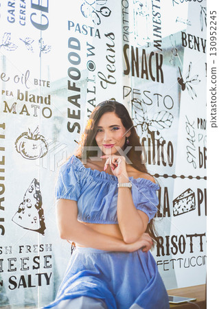 Woman in blue dress poses in a trendy restaurant with a unique wall design Woman in blue dress poses in a trendy restaurant with a unique wall design 130952245