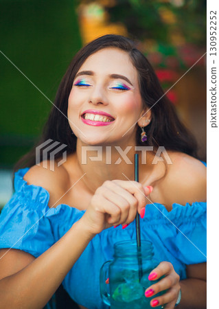 Smiling woman enjoying a colorful drink in a vibrant outdoor cafe during a sunny day Smiling woman enjoying a colorful drink in a vibrant outdoor cafe during a sunny day 130952252