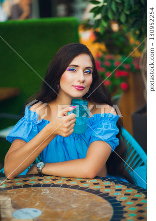 Woman enjoying a refreshing drink at a vibrant outdoor cafe in warm weather Woman enjoying a refreshing drink at a vibrant outdoor cafe in warm weather 130952254