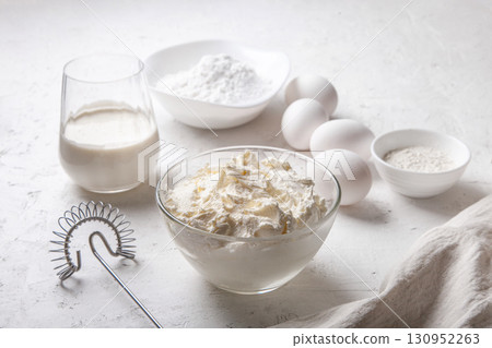 Cream cheese in glass bowl close up with sugar, eggs, flour and cream on light background. Ingredients for cooking Basque Spanish burnt Saint Sebastian cheesecake. Recipe step by step 130952263