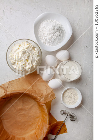 Ingredients for making Basque Spanish burnt Saint Sebastian cheesecake. Cream cheese, sugar, eggs, flour, cream, baking dish covered with paper. Recipe step by step flat lay top view Ingredients for making Basque Spanish burnt Saint Sebastian cheesecake. Cream cheese, sugar, eggs, flour, cream, baking dish covered with paper. Recipe step by step flat lay top view 130952265