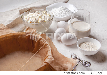 Ingredients for making Basque Spanish burnt Saint Sebastian cheesecake. Cream cheese, sugar, eggs, flour, cream, baking dish covered with paper. Recipe step by step flat lay top view Ingredients for making Basque Spanish burnt Saint Sebastian cheesecake. Cream cheese, sugar, eggs, flour, cream, baking dish covered with paper. Recipe step by step flat lay top view 130952266