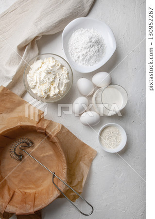 Ingredients for making Basque Spanish burnt Saint Sebastian cheesecake. Cream cheese, sugar, eggs, flour, cream, baking dish covered with paper. Recipe step by step flat lay top view 130952267