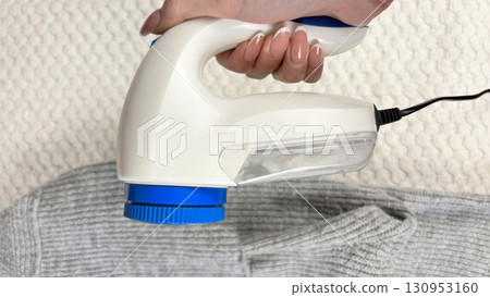 A woman holds a lint remover against a gray warm sweater with bobbles, removing pilling and caring for clothes. Preparing wardrobe for winter and autumn seasons, clothing care and maintenance A woman holds a lint remover against a gray warm sweater with bobbles, removing pilling and caring for clothes. Preparing wardrobe for winter and autumn seasons, clothing care and maintenance 130953160