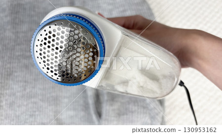 A woman holds a lint remover against a gray warm sweater with bobbles, removing pilling and caring for clothes. Preparing wardrobe for winter and autumn seasons, clothing care and maintenance 130953162
