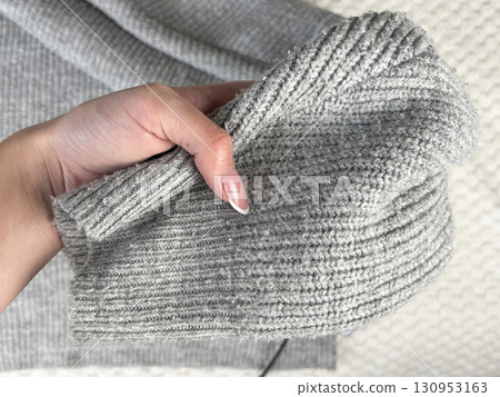 A woman holds the sleeve of a warm gray sweater with bobbles, checking fabric pilling. Preparing and caring for clothes, wardrobe organization for autumn and winter fashion seasons 130953163