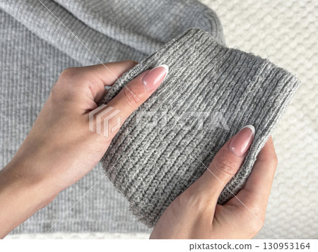 A woman holds the sleeve of a warm gray sweater with bobbles, checking fabric pilling. Preparing and caring for clothes, wardrobe organization for autumn and winter fashion seasons 130953164