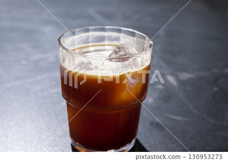 Refreshing iced coffee americano in a clear glass with ice cubes, placed on a dark surface, showcasing the rich color and texture of the beverage, perfect for summer enjoyment Refreshing iced coffee americano in a clear glass with ice cubes, placed on a dark surface, showcasing the rich color and texture of the beverage, perfect for summer enjoyment 130953273
