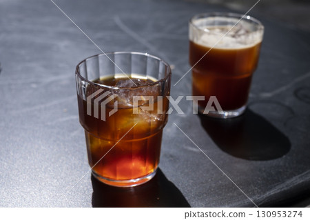 Two glasses of coffee iced americano and cold brew with ice cubes on a dark surface, showcasing rich colors and textures, perfect for summer refreshment and beverage enjoyment 130953274