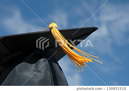 Graduation cap with a bright yellow tassel against a clear blue sky, symbolizing achievement, education, and celebration of academic success in a vibrant outdoor setting 130953318