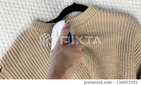 A woman holds a lint remover against a gray warm sweater with bobbles, removing pilling and caring for clothes. Preparing wardrobe for winter and autumn seasons, clothing care and maintenance A woman holds a lint remover against a gray warm sweater with bobbles, removing pilling and caring for clothes. Preparing wardrobe for winter and autumn seasons, clothing care and maintenance 130953393