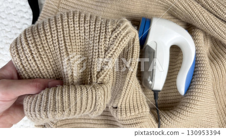 A lint remover against a warm cozy sweater with bobbles. Preparing wardrobe and caring for clothes, clothing care and maintenance, fall and winter fashion and garment preparation 130953394