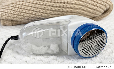 A lint remover against a warm cozy sweater with bobbles. Preparing wardrobe and caring for clothes, clothing care and maintenance, fall and winter fashion and garment preparation 130953397