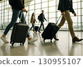 Travelers with luggage walk through a modern airport terminal.. 130955107