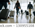 Travelers with luggage walk through a modern airport terminal. 130955108