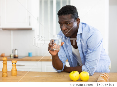 man drinks water after preparing a vegetable salad in the kitchen man drinks water after preparing a vegetable salad in the kitchen 130956104