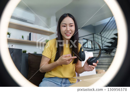 Product showcase. Woman happily displaying headphones in a modern setting. Product showcase. Woman happily displaying headphones in a modern setting. 130956378