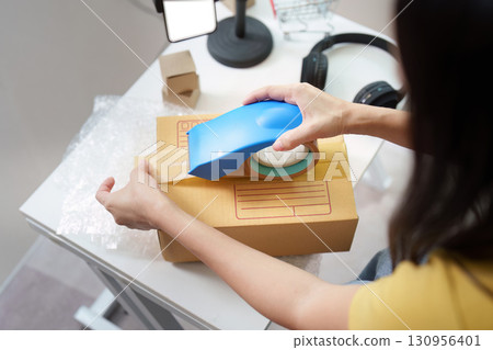 Packaging Essentials. Woman sealing a box with tape for shipping. Packaging Essentials. Woman sealing a box with tape for shipping. 130956401