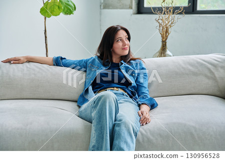 Portrait of relaxed beautiful smiling brunette woman sitting on sofa in living room Portrait of relaxed beautiful smiling brunette woman sitting on sofa in living room 130956528